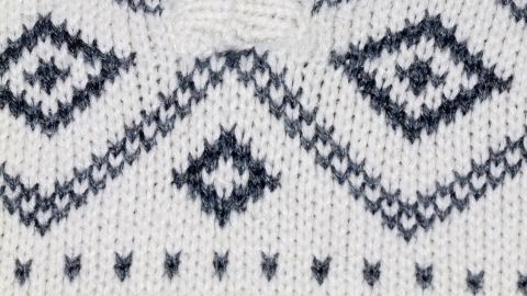Ein weißer Wollpullover mit Zipper und grafischem Muster liegt auf einem Tisch und zeigt seine Textur.