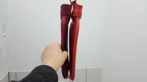 Rote Wärmflasche wird von einer Hand gehalten und schwingt sanft in einem hellen Raum. Ideal für warme Füße im Bett.