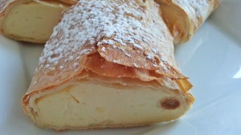 Zarte Topfenstrudel sind auf einem weißen Teller angerichtet, bestäubt mit Puderzucker und zeigen die cremige Füllung.