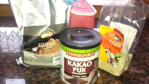 Auf der Arbeitsfläche stehen verschiedene Zutaten: ein Kakaopulverbehälter, Kaffee, Zucker und Gewürze zum Mischen eines koffeinhaltigen Kakaogetränks.
