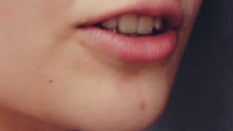 Lippen mit leichtem Herpes sind im Vordergrund zu sehen, während der Hintergrund neutral und unscharf bleibt.