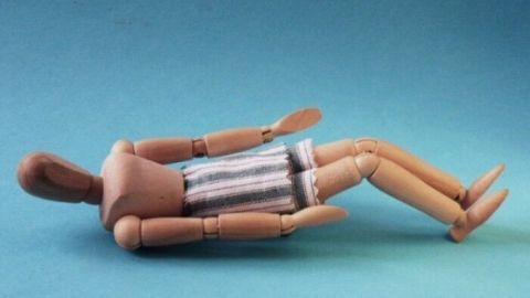 Eine Holzfigur liegt entspannt auf dem Boden und zeigt eine Yoga-Übung zur Förderung der Flexibilität und Balance.