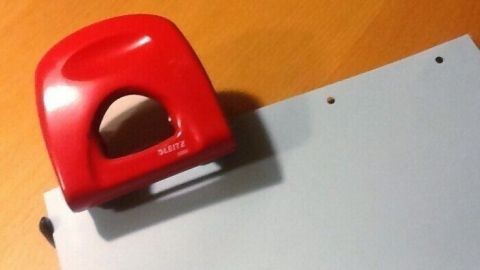 Ein roter Locher stanzt Löcher in ein Blatt Papier, das auf einem Holzschreibtisch liegt.