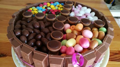 Eine bunte Geburtstagstorte mit verschiedenen Süßigkeiten dekoriert, steht auf einem Tisch und wirkt festlich.