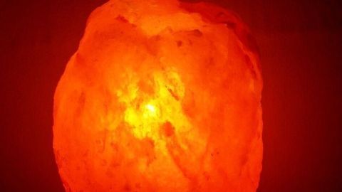 Eine Salzkristalllampe leuchtet sanft rot auf einem Tisch im Schlafzimmer und schafft eine entspannende Atmosphäre.