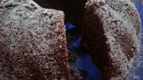 Ein schokoladiger Bundt-Kuchen steht auf einem blauen Teller, mit Puderzucker bestäubt und teils angeschnitten.