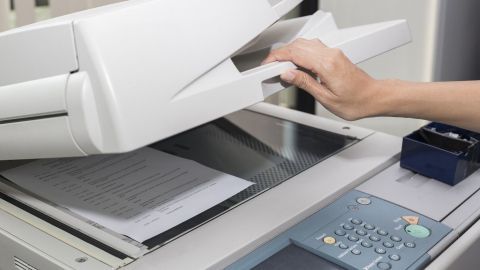 Ein Hand greift Papier aus einem Kopierer, um einseitig bedruckte Blätter für weiteres Drucken zu nutzen.