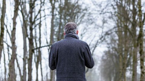 Ein Mann in einem dunklen Mantel geht allein auf einem schmalen Weg durch einen winterlichen Wald, um Winterblues zu bekämpfen.
