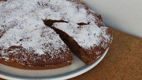 Eine Apfeltarte liegt auf einem Teller, mit Puderzucker best&auml;ubt und teilweise angeschnitten, auf einem Holzuntergrund.