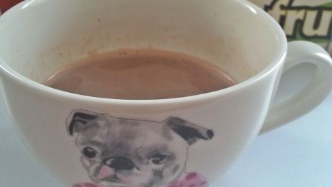 Eine Tasse heiße Schokolade steht auf einem Tisch, dekoriert mit einem Hundemotiv und umgeben von Getränkeflaschen.