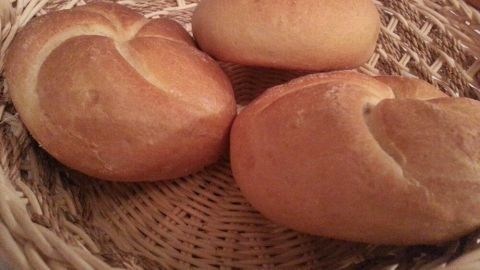 Drei goldbraune Brötchen liegen frisch gebacken in einem geflochtenen Korb auf einem Tisch.