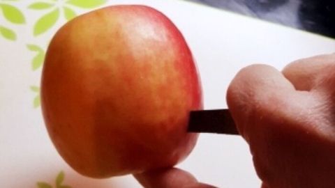 Ein Apfel wird mit einem Messer geschnitten, um mundgerechte Spalten zu kreieren, während eine moderne Küche im Hintergrund sichtbar ist.