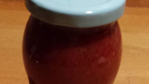 Ein Glas mit selbstgemachtem Ketchup steht auf einer Holzoberfläche, es zeigt eine gesunde, fett- und zuckerarme Variante.