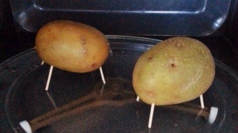 Zwei Kartoffeln stehen auf einem Teller in der Mikrowelle, bereit für eine schnelle Zubereitung als 5-Minuten-Kartoffeln.