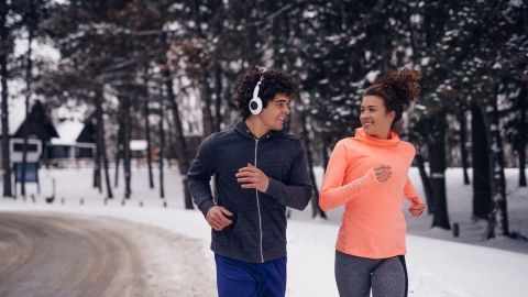 Zwei joggende Personen genießen ihr Outdoor-Training im Winter, umgeben von schneebedeckten Bäumen und einem ruhigen Weg.