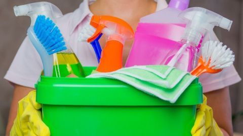 Eine Person mit gelben Handschuhen hält einen grünen Eimer, der mit Reinigungsmitteln für die Haushaltshilfe gefüllt ist.
