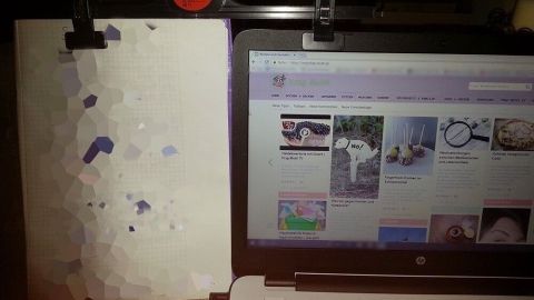 Ein Laptop steht neben einem weißen Blatt Papier, das fixiert ist; der Laptop zeigt eine Webseite mit verschiedenen Inhalten.