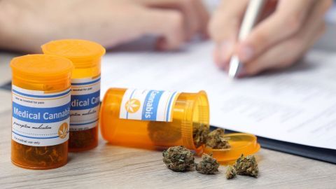 Drei orangefarbige Medikamentendosen liegen neben einer Person, die einen medizinischen Cannabis-Antrag ausfüllt.