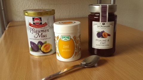 Unter eine "herkömmliche" Pflaumenmarmelade habe ich spontan Zimt-Pulver gemischt - so lange, bis dies meinem Geschmack entsprach, und siehe da: Sie steht dem teuren Produkt in nichts nach! Drei Zutaten stehen auf einem Holzregal: Pflaumenmus, Zimt und ein Glas Marmelade. Ein Löffel liegt bereit zum Mischen.