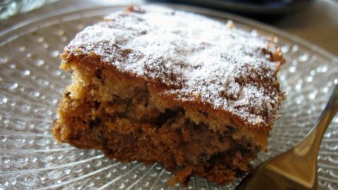 Ein Stück Früchtekuchen liegt auf einem gläsernen Teller, leicht mit Puderzucker bestäubt, bereit zum Genießen.