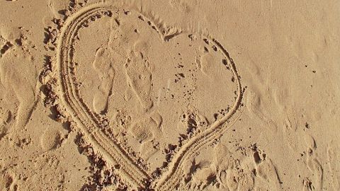 Ein Herz ist im Sand gezeichnet, während die Wellen sanft an den Strand spülen. Perfekt für einen Strandurlaub.