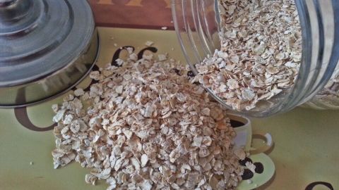 Ein Glas mit Haferflocken steht offen, während die Flocken auf eine grüne Unterlage rieseln, perfekt für ein Frühstückspaket für Lehrer.
