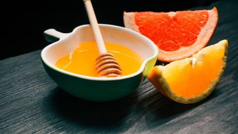 Mit diesem natürlichen Hustensaft bekommt man den Husten schnell in den Griff. Die Herstellung ist sehr einfach. Grapefruitsaft und Honig stehen in einer Schüssel, umgeben von einer Grapefruit und einer Orangenscheibe auf einem dunklen Holzuntergrund.
