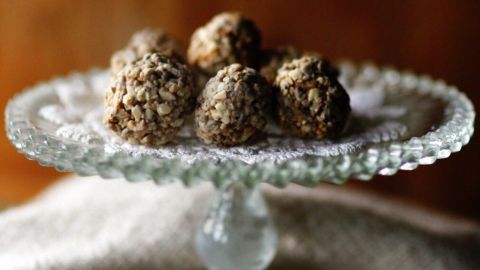 Kleine Müsli-Bällchen aus Hafer und Nüssen liegen appetitlich auf einem eleganten Glasstand, umgeben von einer neutralen Textilie.