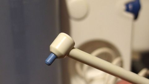 Ein kleiner, weißer Ohrstöpsel wird von einer Hand gehalten, während er vor einem Gerätschaften-Hintergrund positioniert ist.