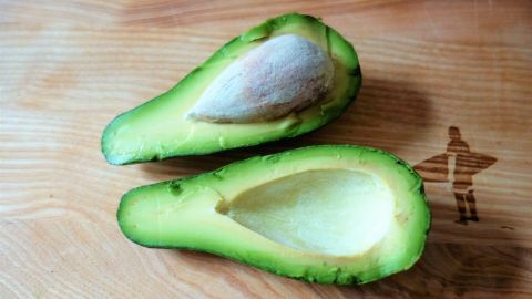 Eine halbierte Avocado liegt auf einem Holztisch, bereit zur Nutzung, während der Avocadokern sichtbar bleibt.
