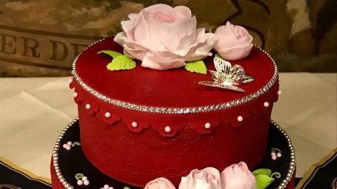 Eine rote Etagentorte mit Blumen und Perlen geschmückt steht elegant auf einem Tisch in festlicher Umgebung.