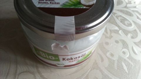 Ein Glas Kokosöl steht auf einem hellen Tisch. Es zeigt das Etikett mit der Aufschrift "Kokosöl nativ".