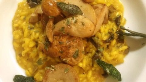 Ein cremiges Risotto mit Steinpilzen und frischen Kräutern auf einem weißen Teller, umgeben von einer eleganten Tischdekoration.