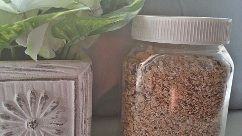 Ein leeres Nutella-Glas steht gefüllt mit Haferflocken neben einer dekorativen Blumenvase auf einem hellen Tisch.