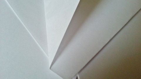 Papierstücke liegen übereinander, während ein schmaler Schnitt sichtbar ist, der mit einem Pflaster behandelt wird.