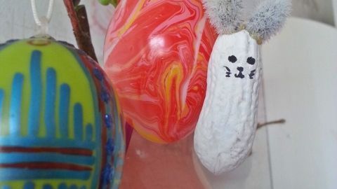 Bunte Erdnuss-Osterhäschen und Eier hängen an einem Strauß, um die fröhliche Osterdeko zu präsentieren.