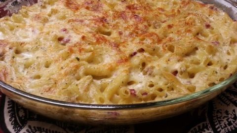 Ein Auflauf mit goldbrauner Kruste, der Pasta und cremiger Sauce kombiniert, steht auf einem bunten Tuch in einer Küche.