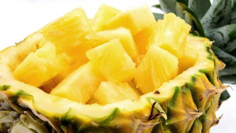 Frische Ananasstücke liegen in einer aufgeschnittenen Ananas, die auf weißem Hintergrund platziert ist.