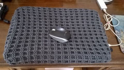 Eine graue Laptop-Abdeckung liegt auf einem Tisch und ein Computer-Maus steht darauf, umgeben von Kabeln und Holzoberfläche.