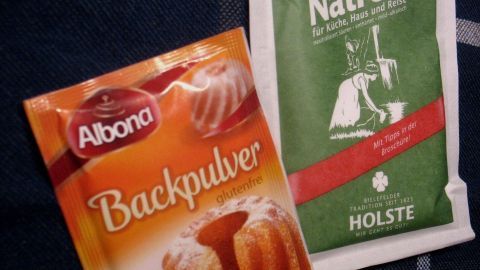 Eine Packung Backpulver liegt neben einer Packung Kaiser-Natron, beide Produkte für das Backen auf einem Tisch.