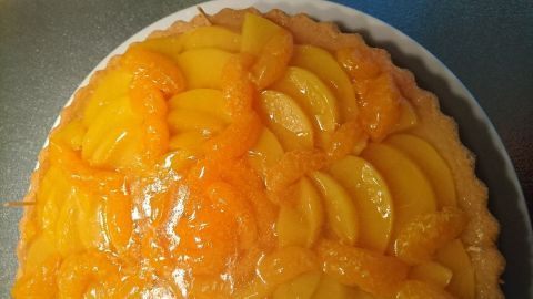 Ein Belegter Tortenboden mit frischen Pfirsichen wird appetitlich präsentiert, auf einem weißen Teller in einer Küche.