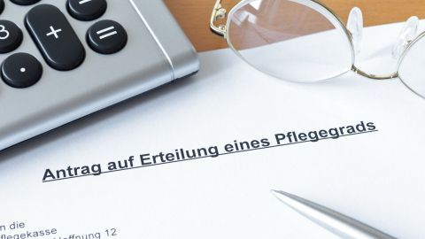 Eine Dokumentenblatt mit dem Titel "Antrag auf Erteilung eines Pflegegrads" liegt auf einem Tisch, neben einer Brille und einem Taschenrechner.