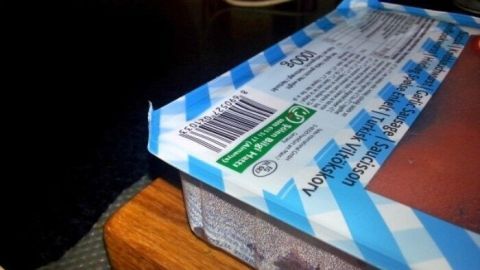 Eine beschädigte Verpackung wird auf einem Tisch betrachtet, möglicherweise um die Suche nach einem neuen Einkaufsbeutel zu thematisieren.
