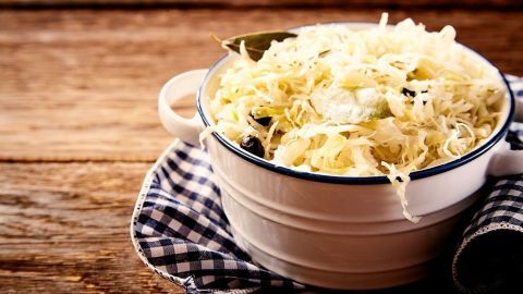 Eine Schüssel mit frisch zubereitetem Sauerkraut steht auf einem Holztisch, umgeben von einem karierten Tuch.