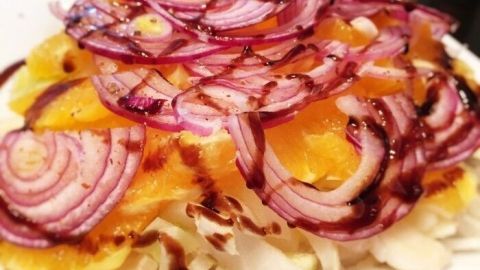 Ein bunter Chicoree-Orangen Salat ist üppig mit roten Zwiebeln bepflanzt und liegt auf einem weißen Teller.