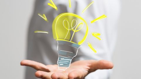 Eine Hand hält eine leuchtende Glühbirne, die Ideen symbolisiert, in einem kreativen, lichtdurchfluteten Umfeld.