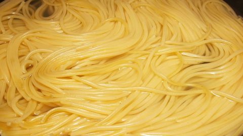 Gekochte Spaghetti liegen in einer Pfanne, umgeben von einem dampfenden Wasserbad, das die Nudeln zart macht.