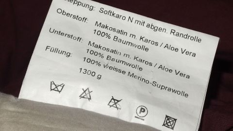 Ein Pflegeetikett zeigt Anweisungen wie "nicht waschen" und Materialhinweise für Textilien in einem Schlafzimmer.