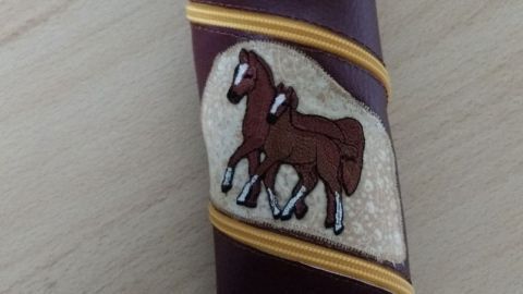 Ein spiralförmiges Mäppchen aus Kunstleder mit einem Pferdemotiv steht auf einem Tisch aus Holz.