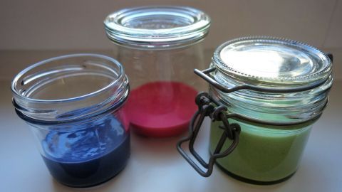 Drei Gläser enthalten selbstgemachte Kinderfarbe in Blau, Rot und Grün und stehen auf einer weißen Oberfläche.